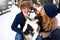 Family portrait of cute happy couple hugging with their alaskan malamute dog licking man`s face. Funny puppy wearing