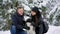 Family portrait of cute happy couple hugging with their alaskan malamute dog licking man`s face. Funny puppy wearing