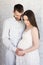 family, pregnancy and parenthood concept - portrait of happy pregnant couple posing over white wall