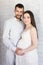 family, pregnancy and parenthood concept - portrait of happy pregnant couple standing over white wall