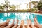 Family relaxing near swimming pool in hotel, feet of group of friends