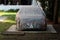 Family sedan car left in backyard on concrete slate covered with grey protective cover surrounded with grass and trees with white