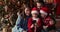 Family sit near decorated Christmas Tree having fun using smartphone