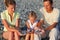 Family sits in pebbly beach and holding pebbles