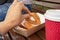 Family sitting on a bench in park and taking beignet pastries, donuts from a paper takeaway box and drinking coffee, street fast