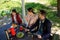 Family Are Sitting By The Table In Wooden Gazebo In Park While Looking On The Left Side.