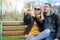 The family speaks on video call. Husband and wife are sitting on a swing in the park and have fun talking on a smartphone with