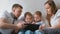 Family with tablet. Mom, dad and two sons twins toddlers looking cartoon at tablet lying on the bed.