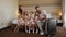 Family with their son and twin girls sit on a hotel bed next to a large suitcase