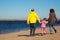 Family of three people walking along beach.