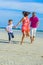 Family of three running along the tropical beach, laughing and enjoing time together.