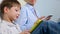 A family of three sit on the couch and uses digital devices. The boy using tablet and mother browsing information on the