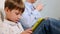 A family of three sit on the couch and uses digital devices. The boy using tablet and mother browsing information on the