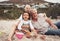 Family, time and beach with grandparents and grandchild laugh and play in sand, sitting and bonding in nature. Portrait