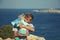 Family of travelers. Father hugging and kisses his toddler son while standing on the edge of rocky seashore, with tourist map in