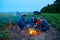 Family traveling and camping, twilight, cooking on the fire. Beautiful nature - field, forest and moon