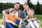 Family with two children holding badminton racquets and smiling at camera outdoors