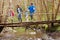 Family Walking Across Wooden Bridge Over Stream In Forest