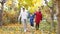 Family walks letting little son to jump along autumn park