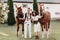 A family in white clothes with their son stand near two beautiful horses in nature. A stylish couple with a child are photographed