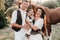 A family in white clothes with their son stand near two beautiful horses in nature. A stylish couple with a child are photographed