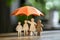 A Family of Wooden Figures Sheltered Underneath a Small Orange Umbrella on a Table