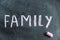 Family. A word written in pink chalk on a black chalkboard. Handwritten text. A piece of colored chalk hangs next to it