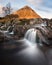 Famous Glencoe waterfall with The Buachaille in the background. Taken on a sunny morning with light hitting the mountain peak.
