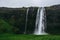 Famous Seljalandsfoss waterfall in Iceland. Saturated green grass, pale gray rocks, heavy rainy sky