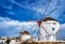 Famous tourist attraction of Mykonos, Greece. Two traditional whitewashed windmills by waterfront and town. Summer