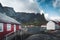 Famous tourist attraction of Reine in Lofoten, Norway with red rorbu houses, clouds, rainy day with bridge and grass and