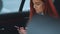 Fantastic attractive young red-haired girl with smartphone smiling and sitting on the back seat of the car using her