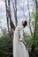 Fantastic fairy beautiful woman in white long dress on old dry tree. Girl princess in swamp. Fashion model sexy girl posing on a