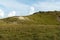 Fantastic view from below of hill and clouds on a sunny day. Grass, trees and many stones grow on hill. Small stones pour down in