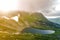 Fantastic wide peaceful view of blue lake in green valley and small tourist tents at rocky mountain with patches of snow covered