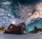 Fantastic winter landscape with wooden house with light in window in snowy mountains and Northern light in night sky. Christmas