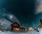 Fantastic winter landscape with wooden house with light in window in snowy mountains and Northern light in night sky. Christmas