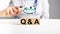 FAQ in health and medicine. Doctor holding magnifier over wooden blocks with letters q a. Woman with stethoscope answers
