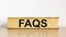 FAQS, frequently asked questions symbol. Book with word `FAQS, frequently asked questions` on beautiful wooden table, white