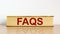 FAQS, frequently asked questions symbol. Book with word `FAQS, frequently asked questions` on beautiful wooden table, white