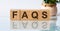 FAQS is a word written in black letters on wooden cubes located on a white mirror surface