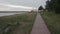 Faraway view of girl standing on wooden path near river. Windy weather. Slow motion,