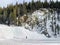 A faraway view of a person hiking alone in a snowy valley surrounded by forests and mountains