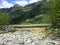 A faraway view of power lines running through a forest on the side of a mountain beside an inlet.