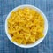 Farfalle macaroni Pasta in a white cup on a blue knitted background in the center. Close-up with the top.