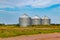 Farm produce storage system. Three corrugated metal clad storage bins.