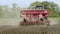 Farm tractor with trailer seeder sowing on plowed land. Cultivated field