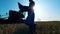 Farm worker stands near a tractor in field, typing on laptop.