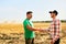 Farmer and agronomist shaking hands in wheat field after agreement. Agriculture business contract concept. Corporate