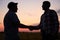 Farmer and agronomist silhouettes shaking hands standing in a wheat field after agreement in dusk. Agriculture business